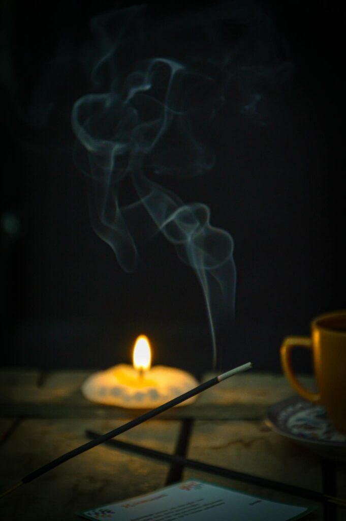 Atmospheric indoor setting with candlelight, incense smoke, and a warm beverage.