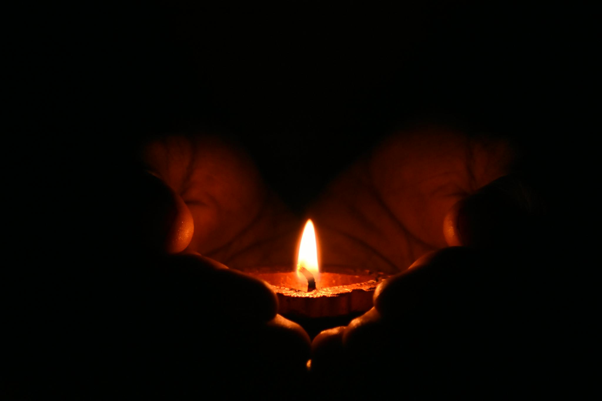 Close-up of hands warmly embracing a lit candle in the dark, creating a cozy atmosphere.